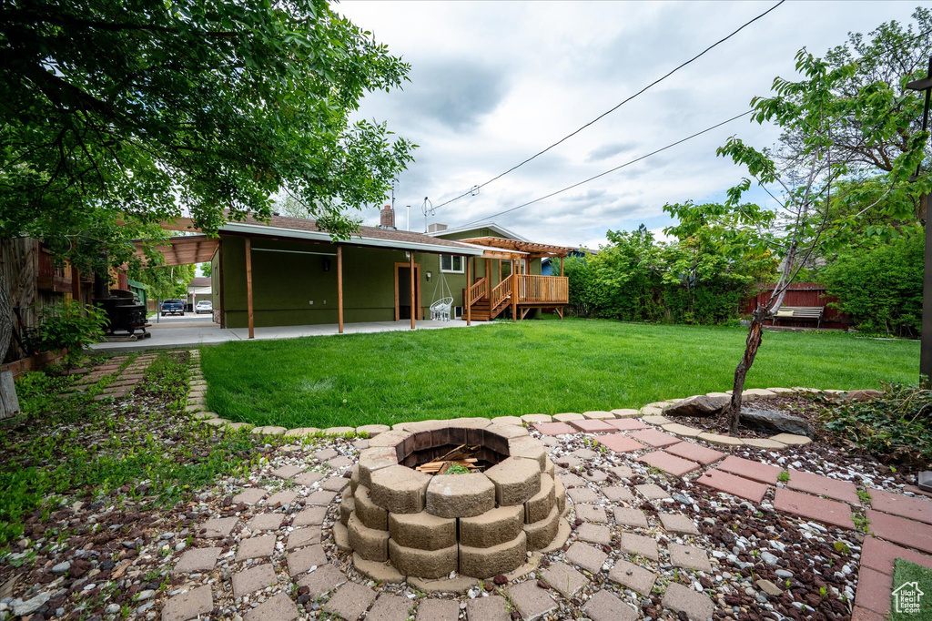 View of green lawn with a fire pit and a wooden deck