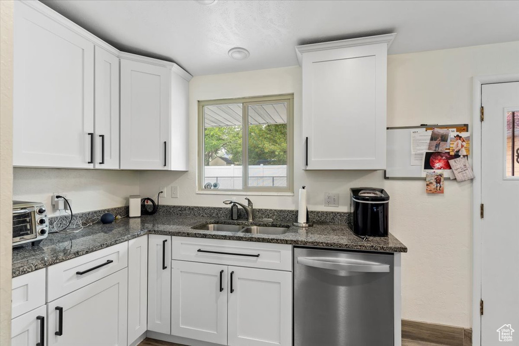 Kitchen with stainless steel dishwasher, a sink, white cabinetry, and dark stone countertops
