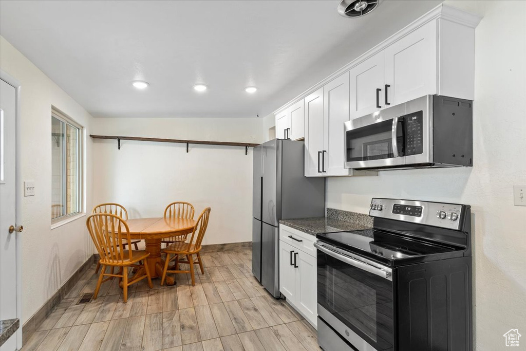 Kitchen with appliances with stainless steel finishes, white cabinets, baseboards, recessed lighting, and light wood finished floors