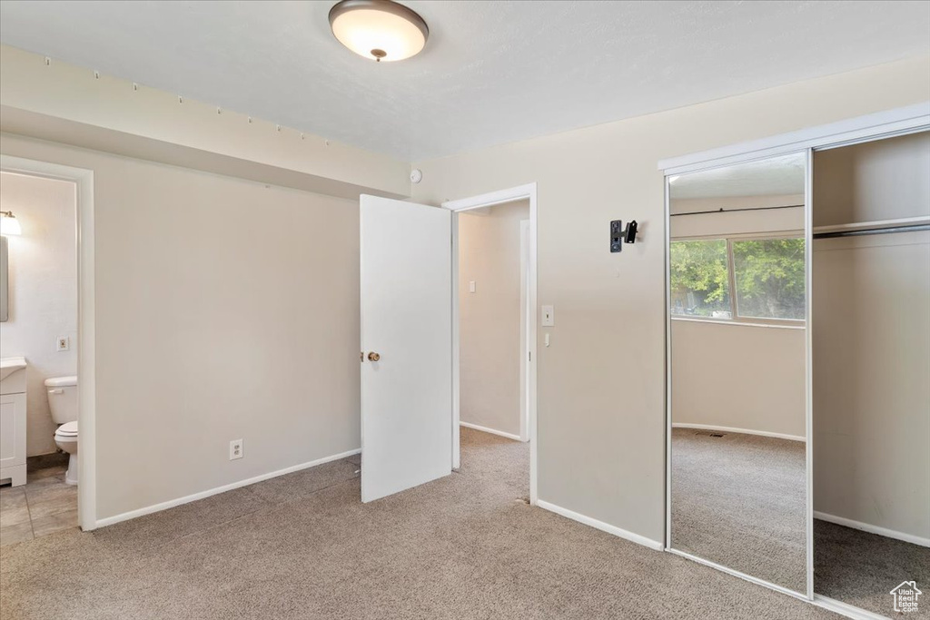 Unfurnished bedroom featuring a closet, light carpet, baseboards, and connected bathroom