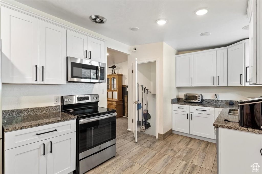Kitchen with appliances with stainless steel finishes, white cabinetry, dark stone counters, recessed lighting, and light wood-style floors