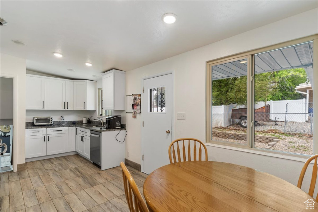 Kitchen with stainless steel dishwasher, a sink, white cabinets, dark countertops, and recessed lighting