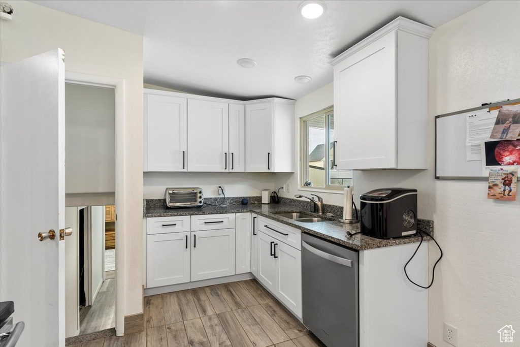 Kitchen featuring stainless steel dishwasher, a sink, white cabinets, and dark stone counters