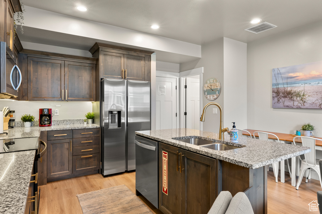 Kitchen with a sink, stainless steel appliances, light wood-style floors, dark brown cabinets, and recessed lighting
