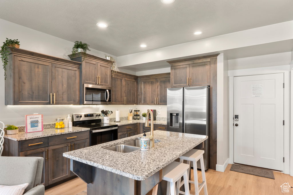 Kitchen with stainless steel appliances, a sink, light wood finished floors, a kitchen breakfast bar, and dark brown cabinetry