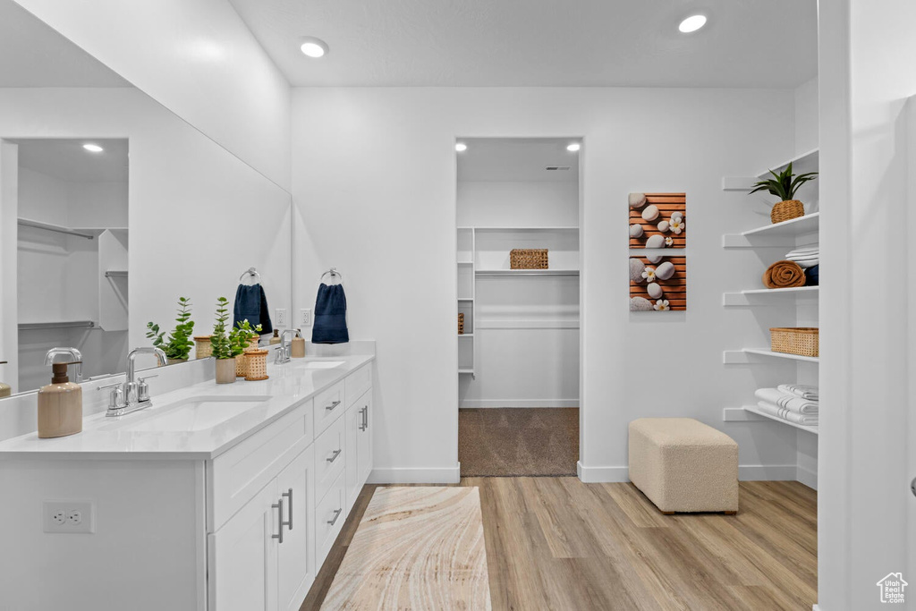 Bathroom with wood finished floors, double vanity, a walk in closet, recessed lighting, and baseboards