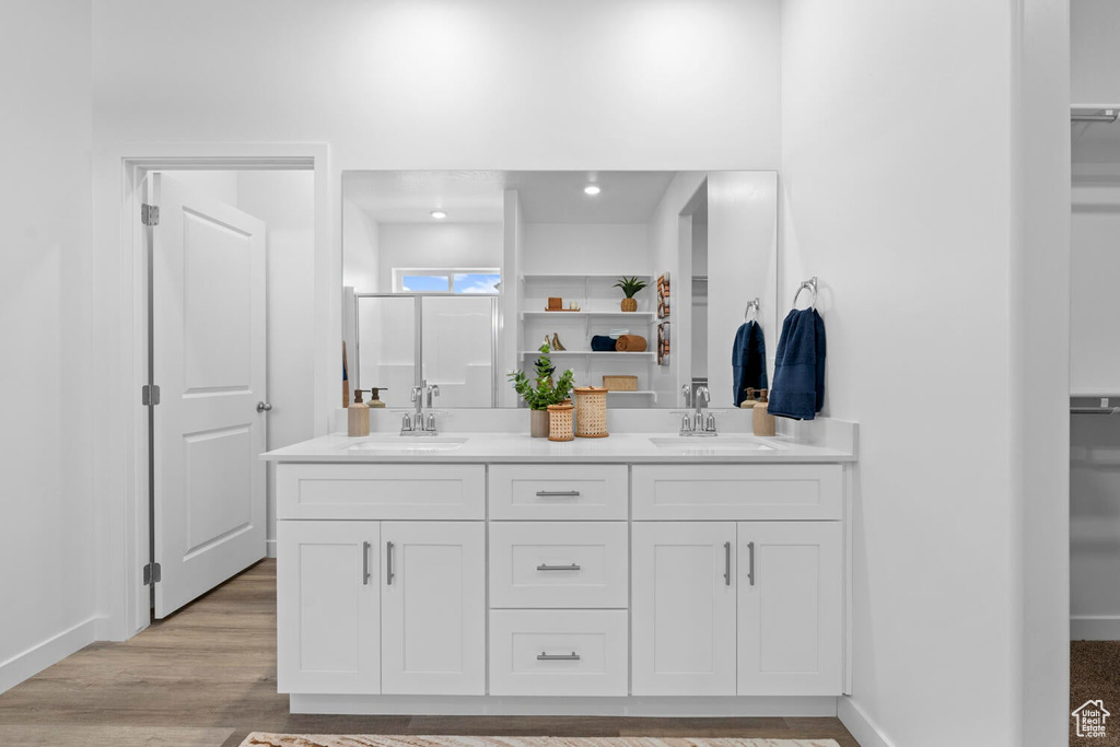 Full bathroom featuring a walk in closet, double vanity, baseboards, and wood finished floors