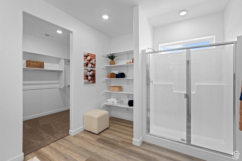 Bathroom with a stall shower, a spacious closet, wood finished floors, and recessed lighting