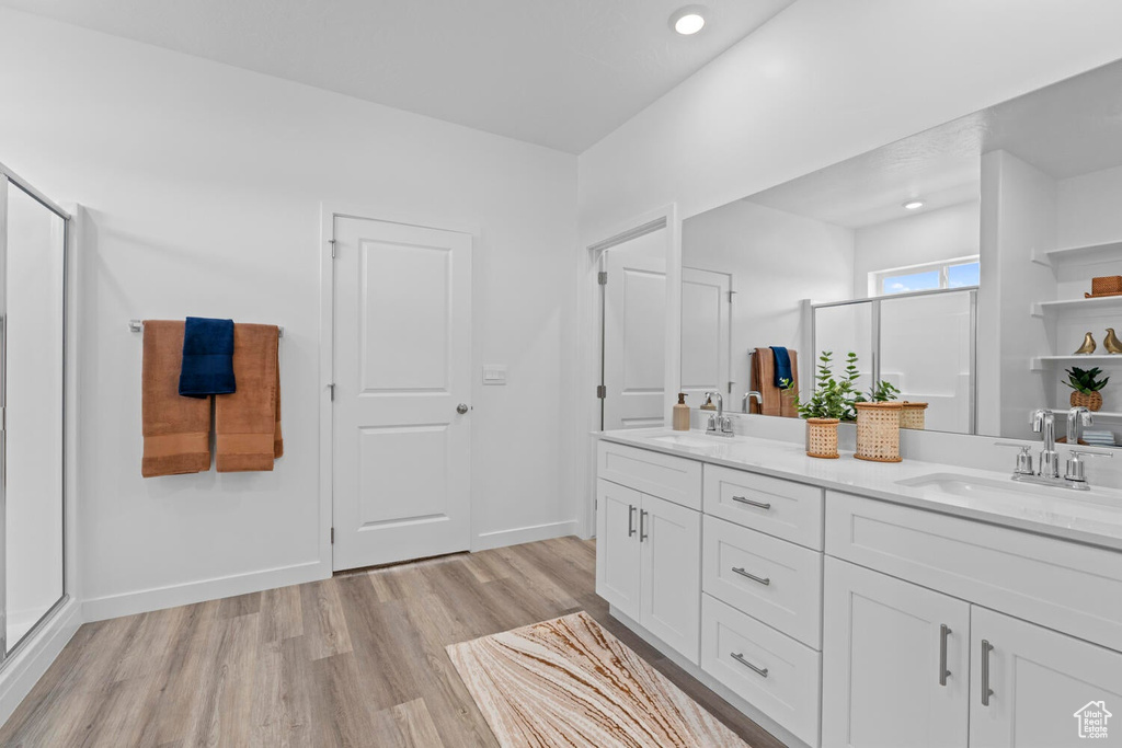 Full bath with wood finished floors, a stall shower, double vanity, recessed lighting, and baseboards