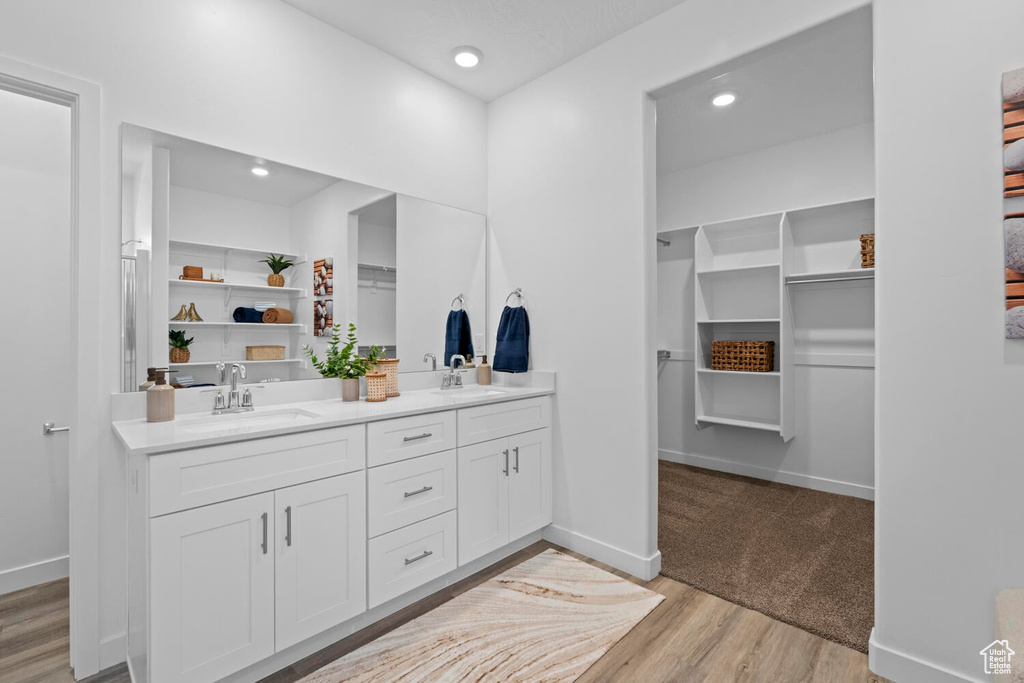 Full bath with wood finished floors, a spacious closet, double vanity, baseboards, and recessed lighting