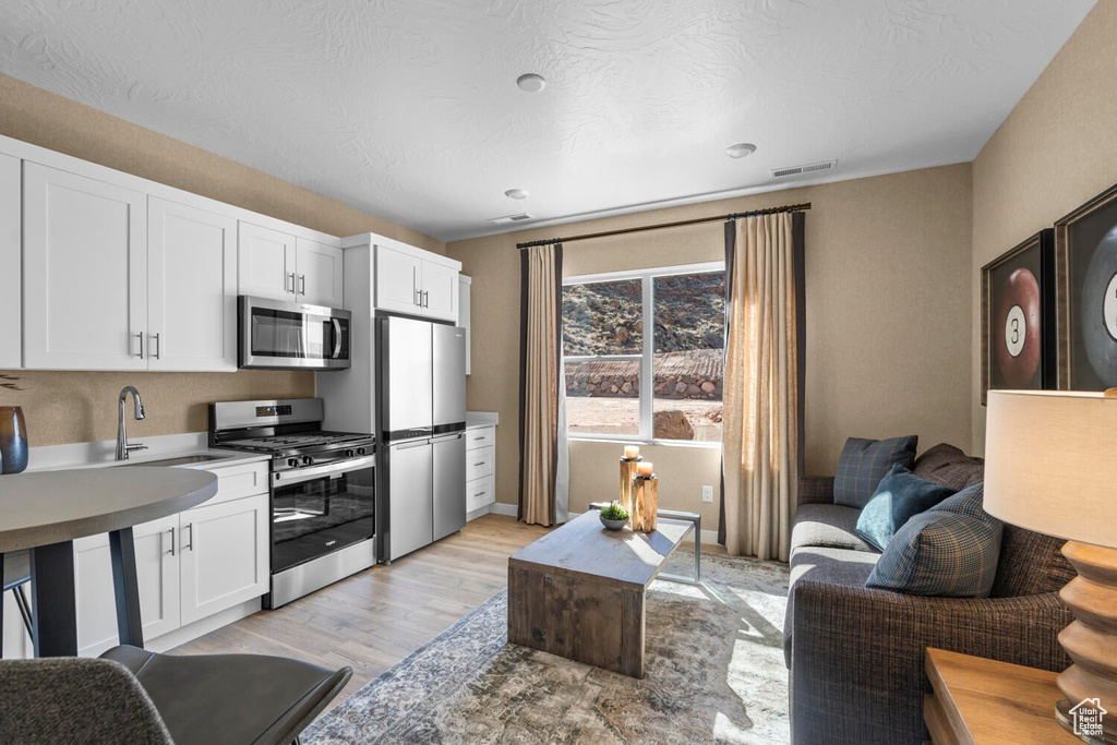 Kitchen with stainless steel appliances, light wood finished floors, white cabinetry, a sink, and baseboards