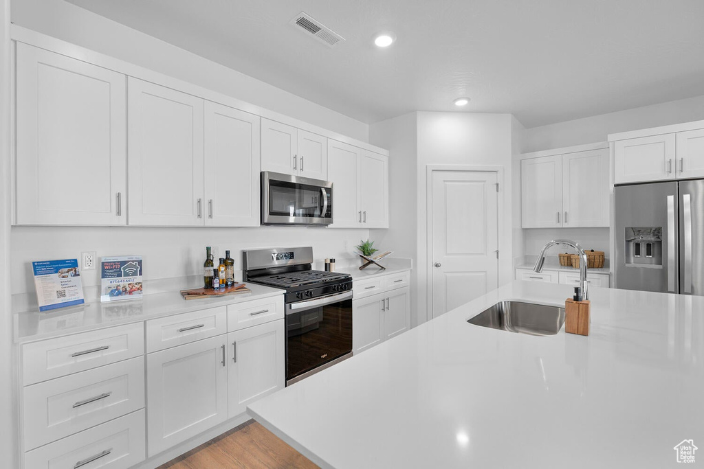 Kitchen featuring appliances with stainless steel finishes, a sink, light countertops, recessed lighting, and white cabinets