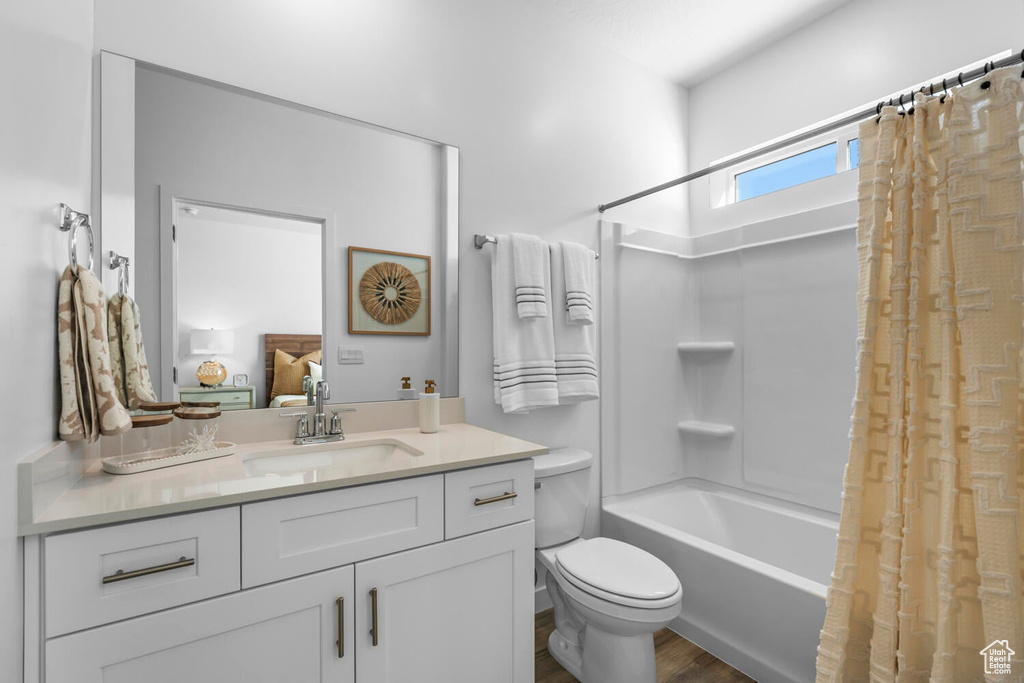 Bathroom with shower / bath combo with shower curtain, vanity, wood finished floors, and toilet