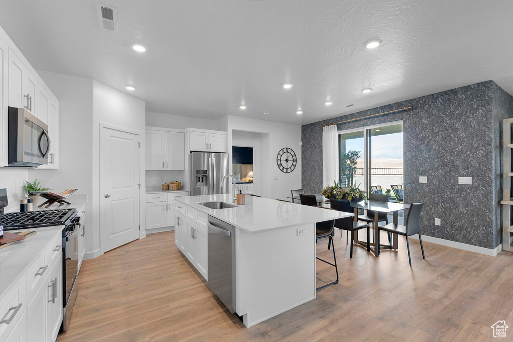 Kitchen featuring stainless steel appliances, a sink, recessed lighting, light wood finished floors, and an island with sink