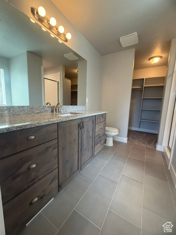 Bathroom with vanity, tile patterned flooring, baseboards, toilet, and a spacious closet