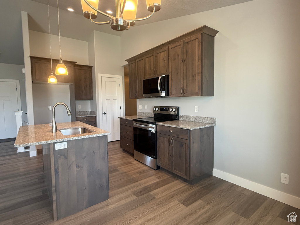 Kitchen featuring stainless steel appliances, a sink, dark wood-style floors, light stone counters, and baseboards