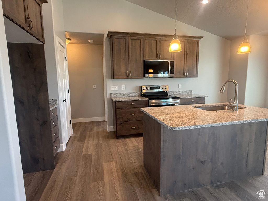 Kitchen featuring stainless steel appliances, a sink, vaulted ceiling, wood finished floors, and decorative light fixtures