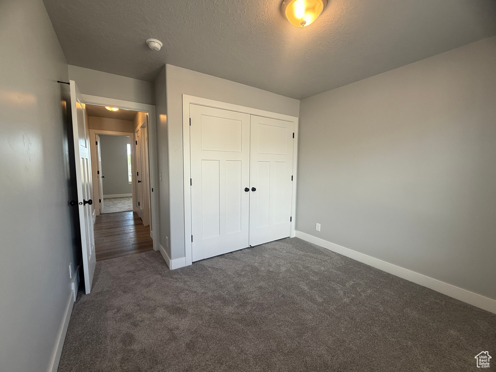 Unfurnished bedroom with baseboards, dark colored carpet, a closet, and a textured ceiling