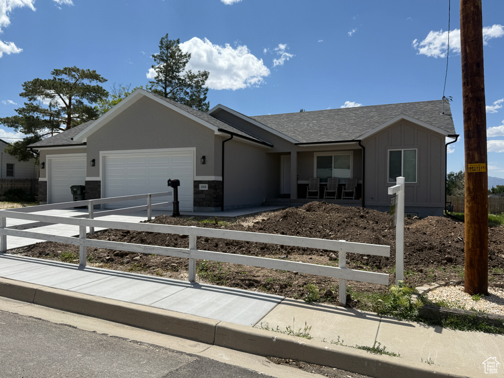 Ranch-style house featuring an attached garage, a fenced front yard, board and batten siding, concrete driveway, and roof with shingles