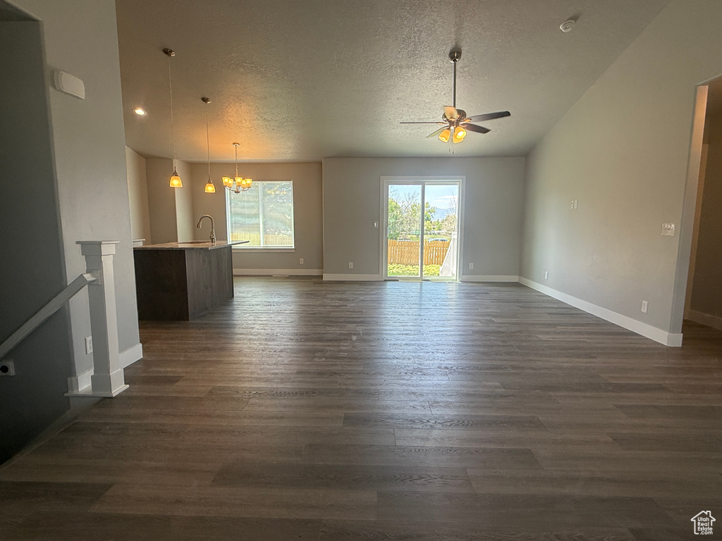 Unfurnished living room featuring ceiling fan, a textured ceiling, a chandelier, dark wood-style floors, and baseboards