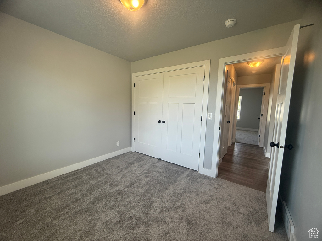 Unfurnished bedroom with dark colored carpet, baseboards, a closet, and a textured ceiling