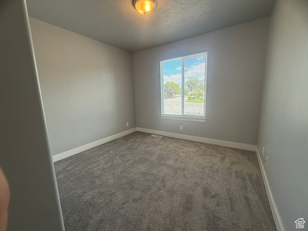 Unfurnished room featuring baseboards, dark colored carpet, and a textured ceiling