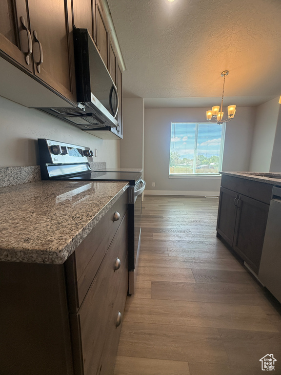 Kitchen featuring stainless steel appliances, light wood-style flooring, baseboards, a textured ceiling, and a chandelier