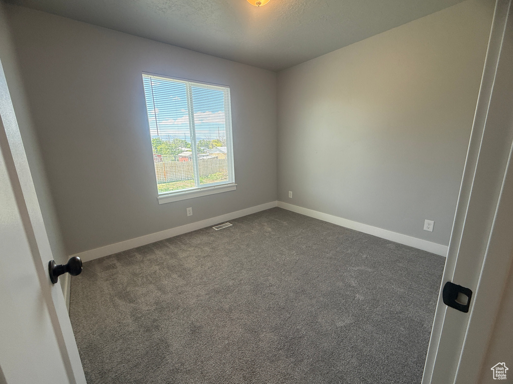 Spare room featuring dark carpet, baseboards, and a textured ceiling