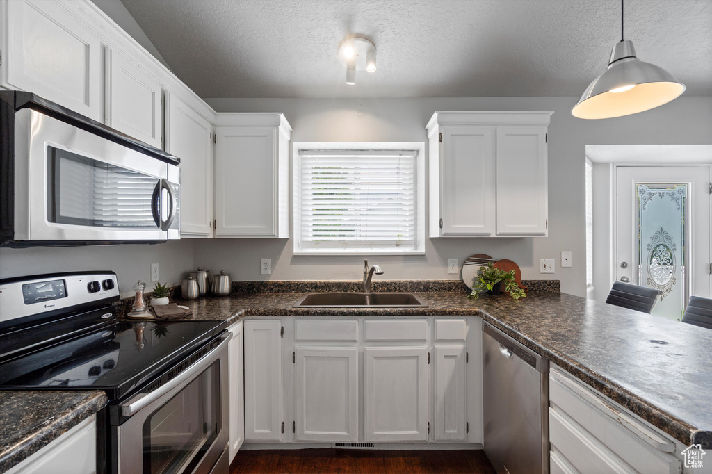 Kitchen with appliances with stainless steel finishes, a sink, white cabinets, dark countertops, and a textured ceiling