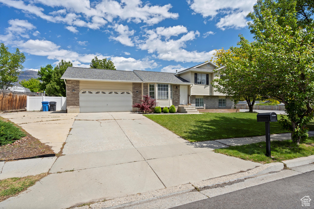 Split level home featuring brick siding, an attached garage, driveway, and roof with shingles