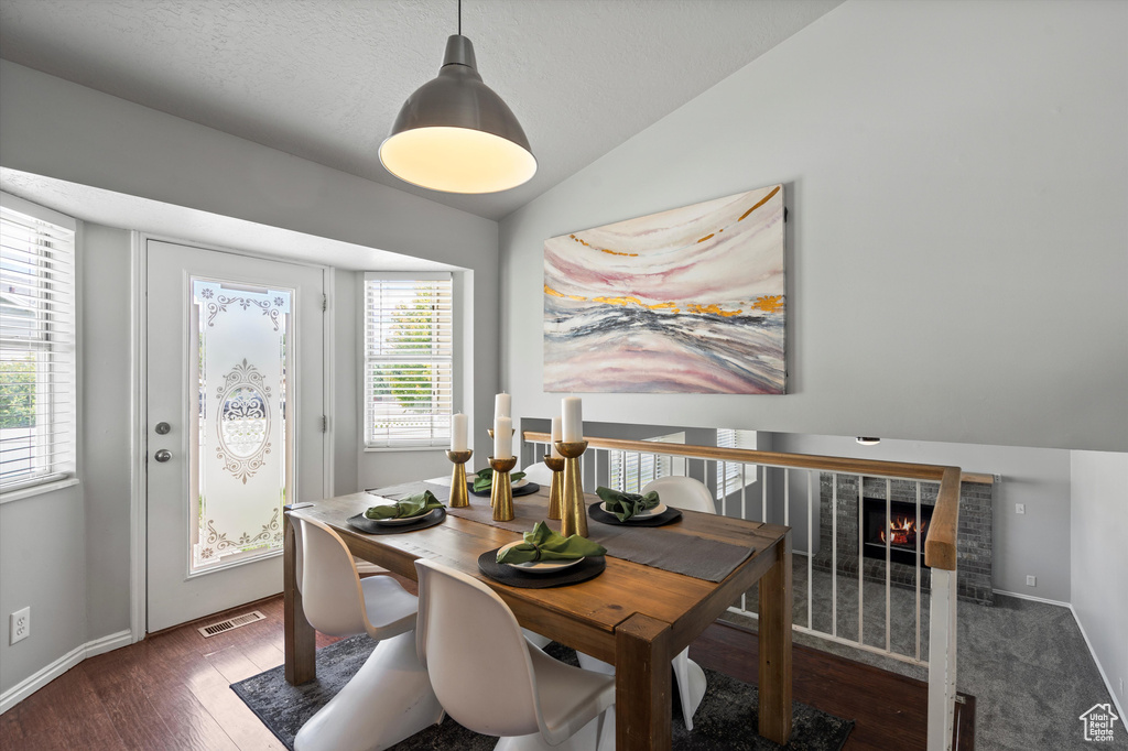 Dining area featuring lofted ceiling, wood finished floors, baseboards, and a brick fireplace