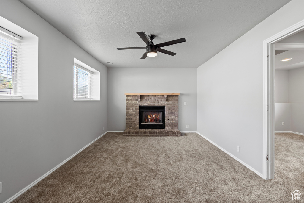 Unfurnished living room featuring carpet floors, ceiling fan, a fireplace, a textured ceiling, and baseboards