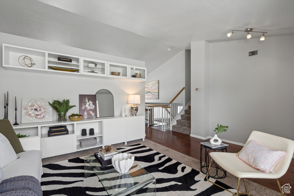 Living room with wood finished floors, stairs, vaulted ceiling, and baseboards