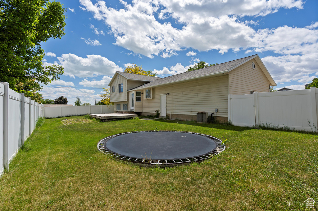 Back of property featuring a trampoline, a deck, cooling unit, and a shingled roof