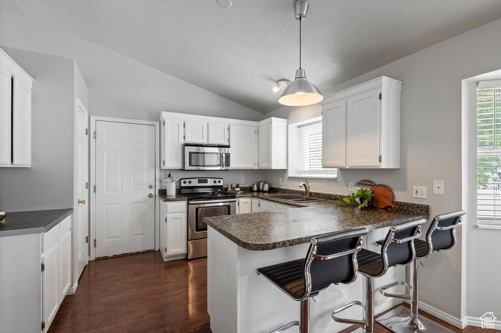 Kitchen featuring appliances with stainless steel finishes, a sink, dark countertops, white cabinetry, and a peninsula