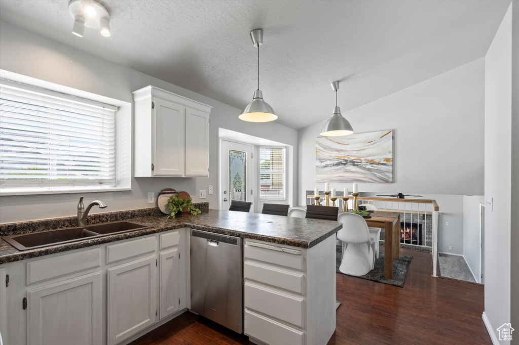 Kitchen with dishwasher, a sink, dark countertops, a peninsula, and white cabinetry
