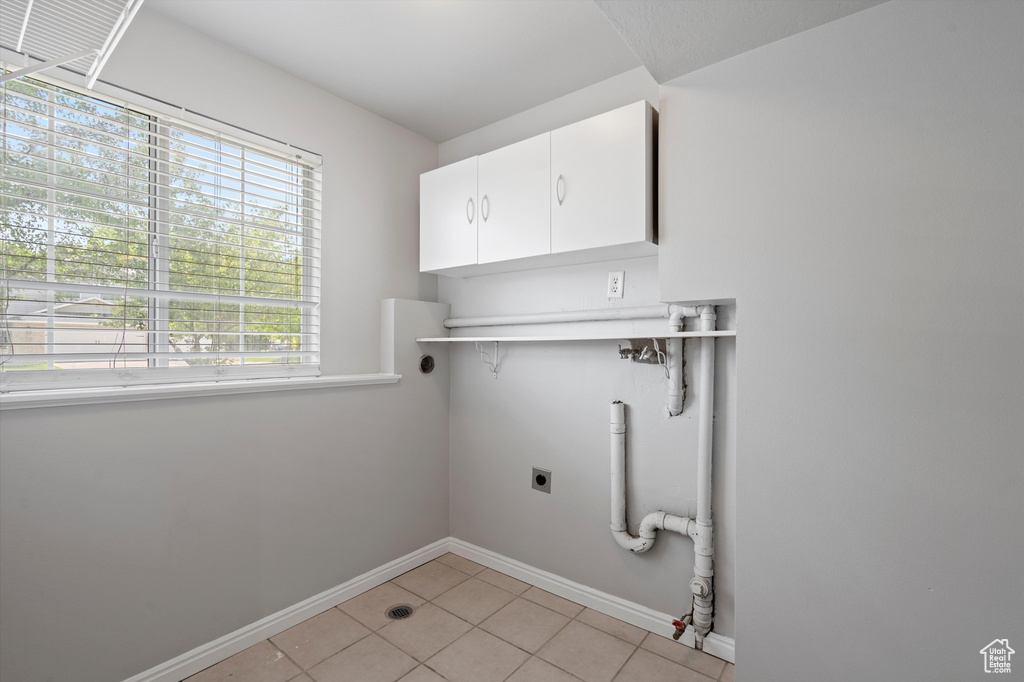 Laundry room with cabinet space, electric dryer hookup, light tile patterned floors, and baseboards