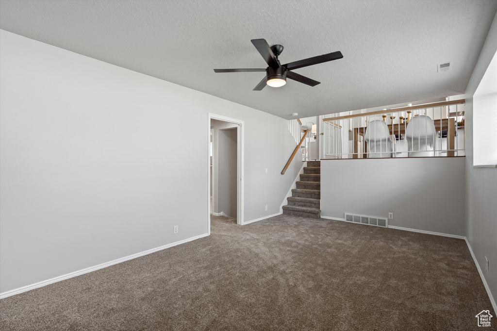 Unfurnished room with ceiling fan, carpet floors, baseboards, stairway, and a textured ceiling