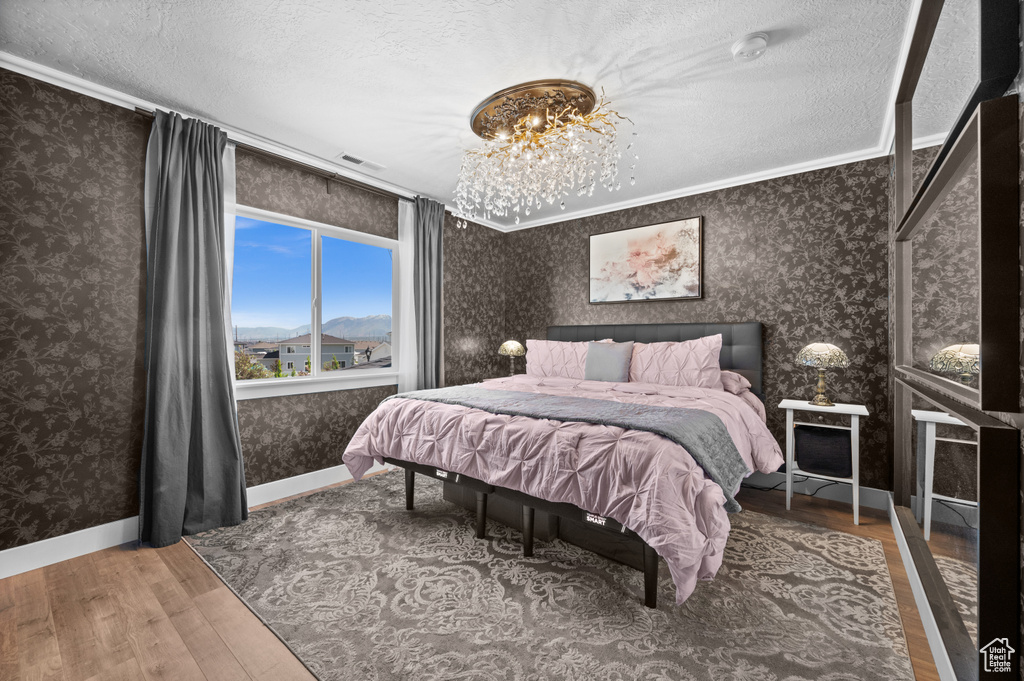 Bedroom featuring wallpapered walls, wood finished floors, ornamental molding, baseboards, and a textured ceiling