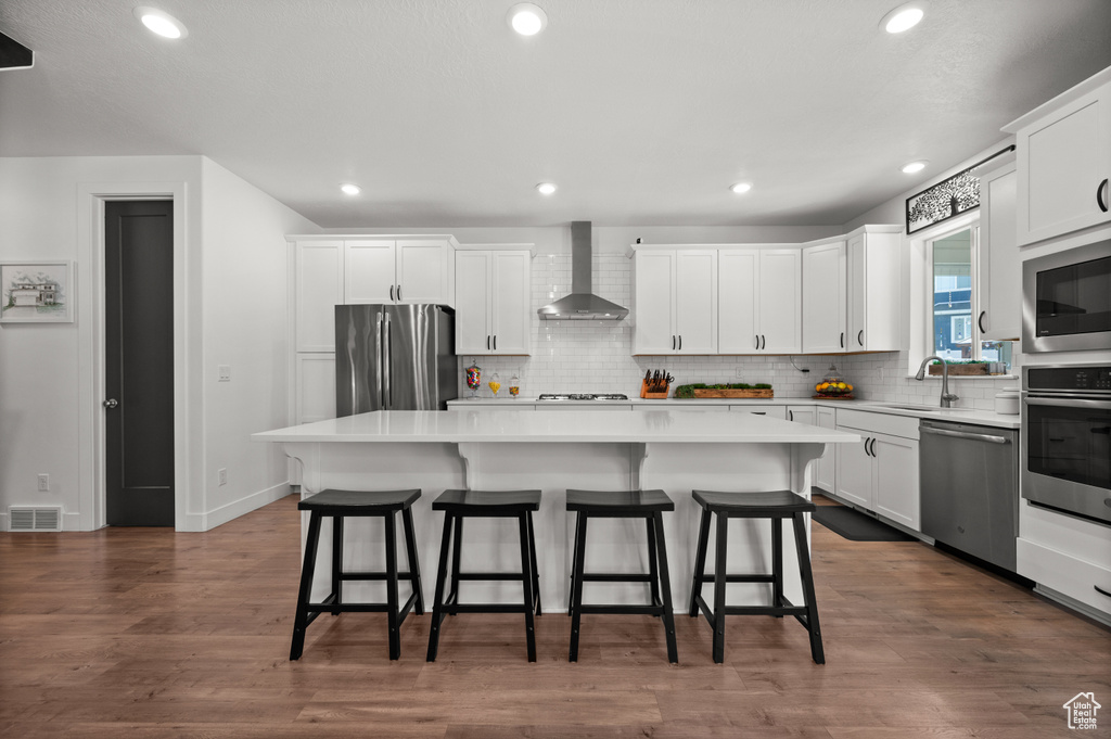Kitchen featuring appliances with stainless steel finishes, wall chimney range hood, a sink, a center island, and tasteful backsplash