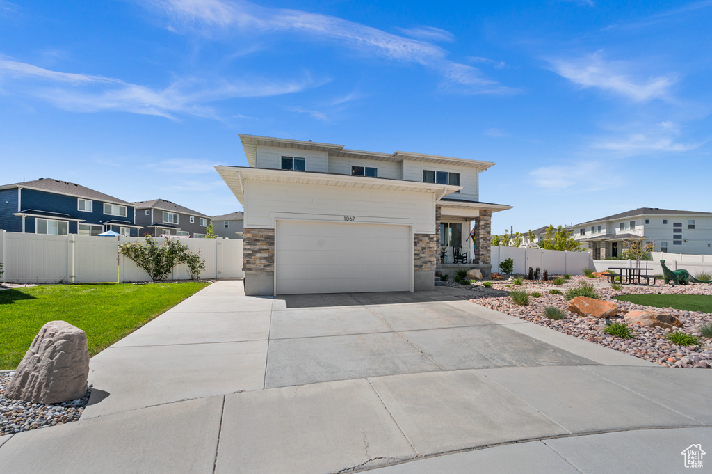 View of front of property with stone siding, driveway, an attached garage, and a residential view