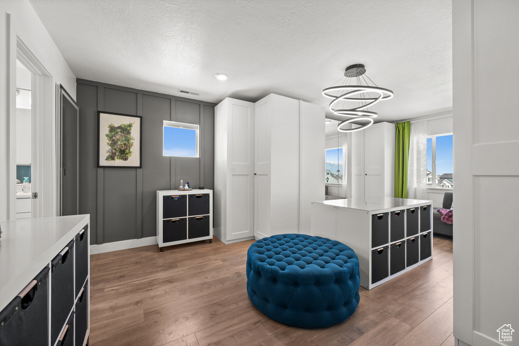 Living area with a chandelier, light wood finished floors, a decorative wall, and a textured ceiling