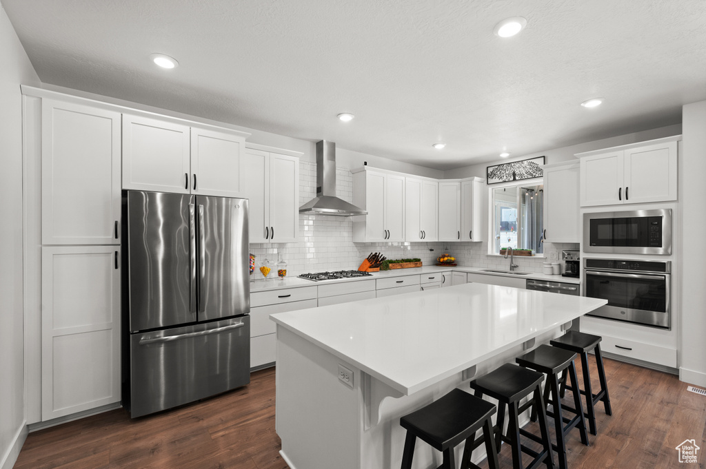 Kitchen featuring appliances with stainless steel finishes, wall chimney exhaust hood, a sink, decorative backsplash, and recessed lighting