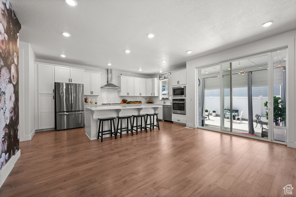 Kitchen with appliances with stainless steel finishes, wall chimney exhaust hood, a breakfast bar area, white cabinets, and light countertops
