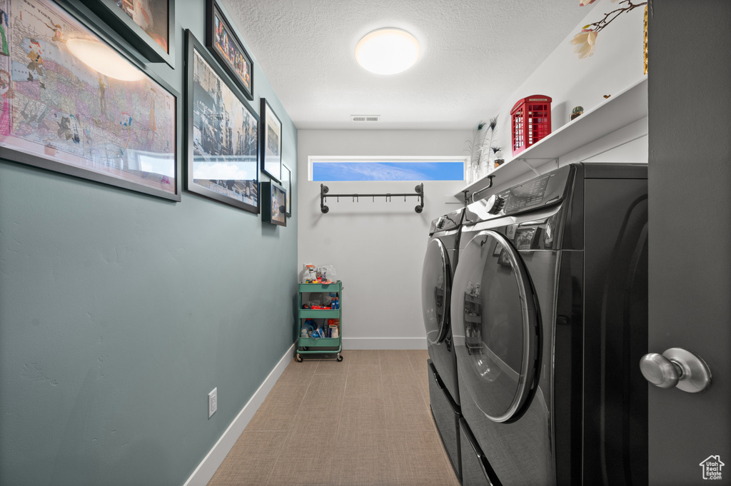 Laundry area with washer and dryer, light carpet, a textured ceiling, and baseboards
