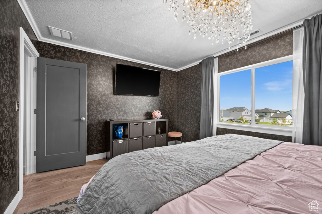 Bedroom featuring wood finished floors, a chandelier, a textured ceiling, wallpapered walls, and crown molding