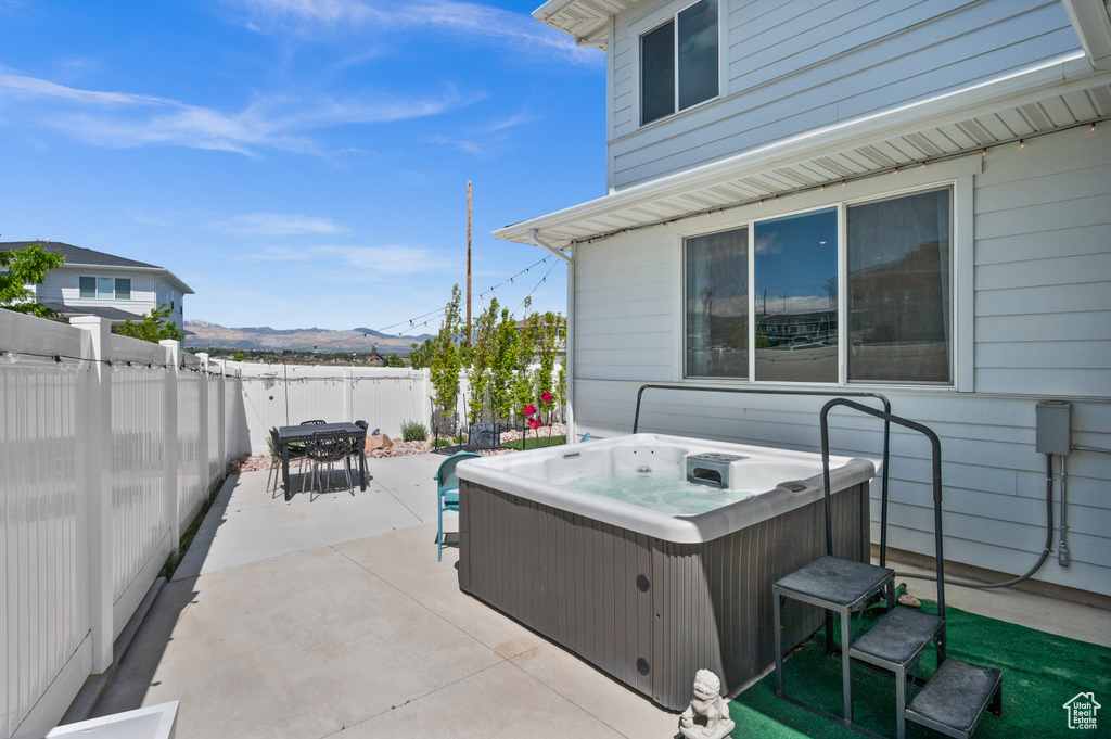 Fenced backyard featuring a hot tub, a patio, outdoor dining space, and a mountain view