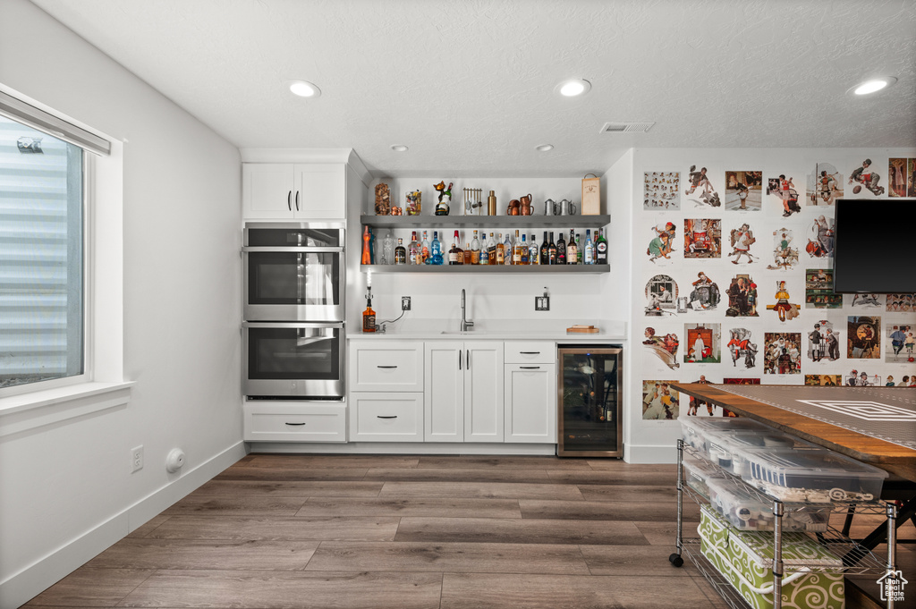 Indoor wet bar with beverage cooler, double oven, plenty of natural light, wood finished floors, and recessed lighting