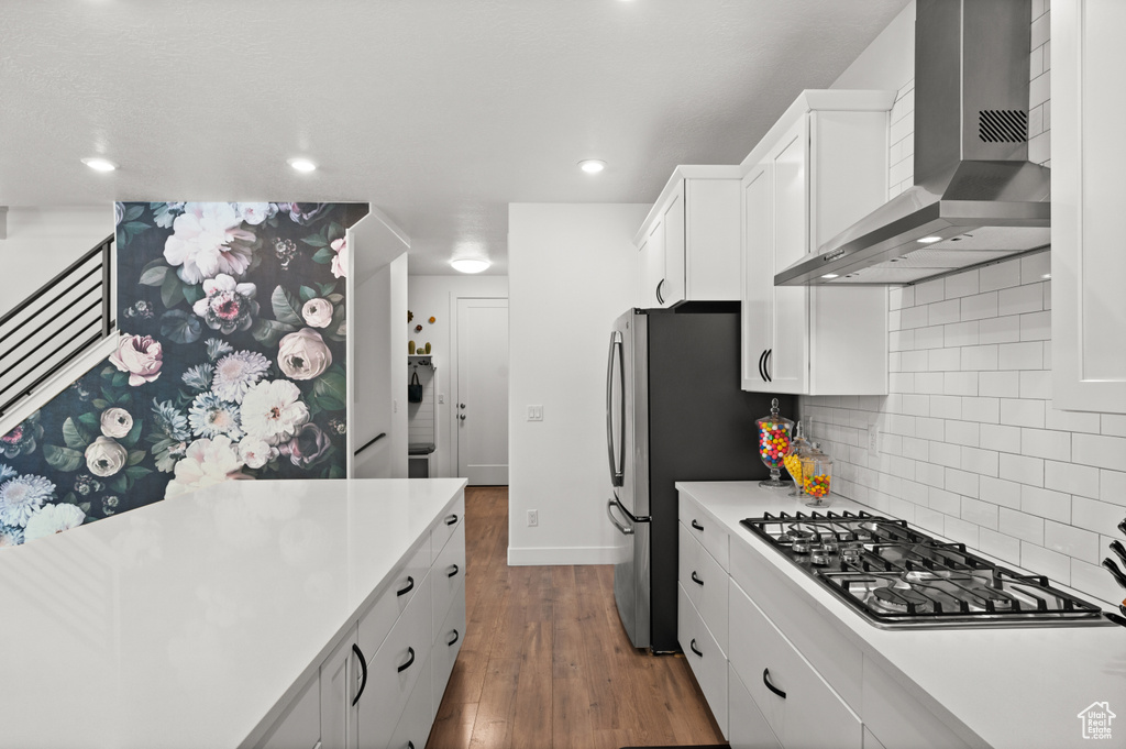 Kitchen featuring wall chimney range hood, appliances with stainless steel finishes, dark wood finished floors, light countertops, and backsplash