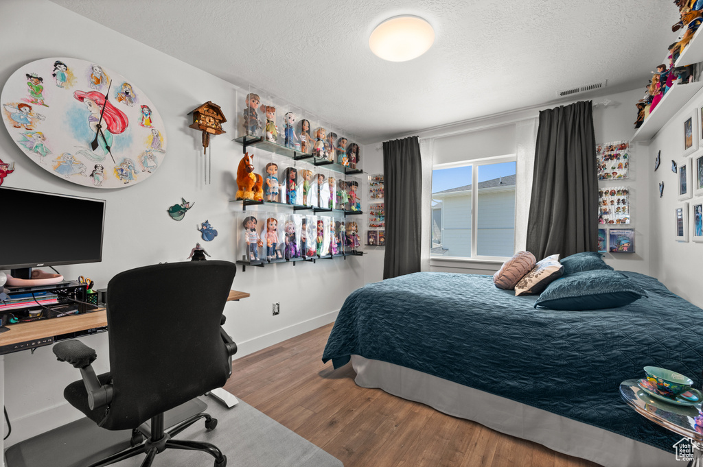 Bedroom featuring wood finished floors, a textured ceiling, a desk, and baseboards